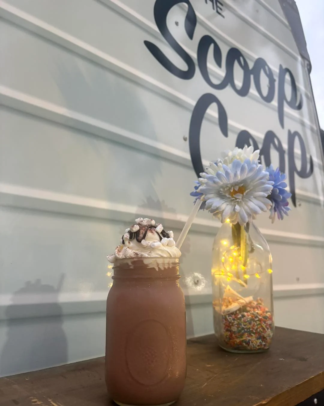 Chocolate milkshake in a mason jar with whipped cream and mini-marshmallows beside a flower arrangement
