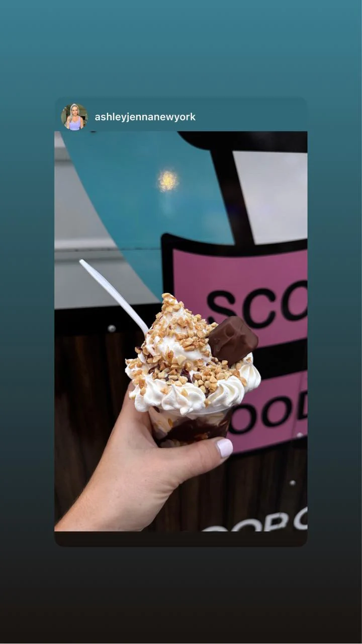 Hand-held Snickers sundae topped with whipped cream, peanuts, and a Snickers piece, in front of the truck
